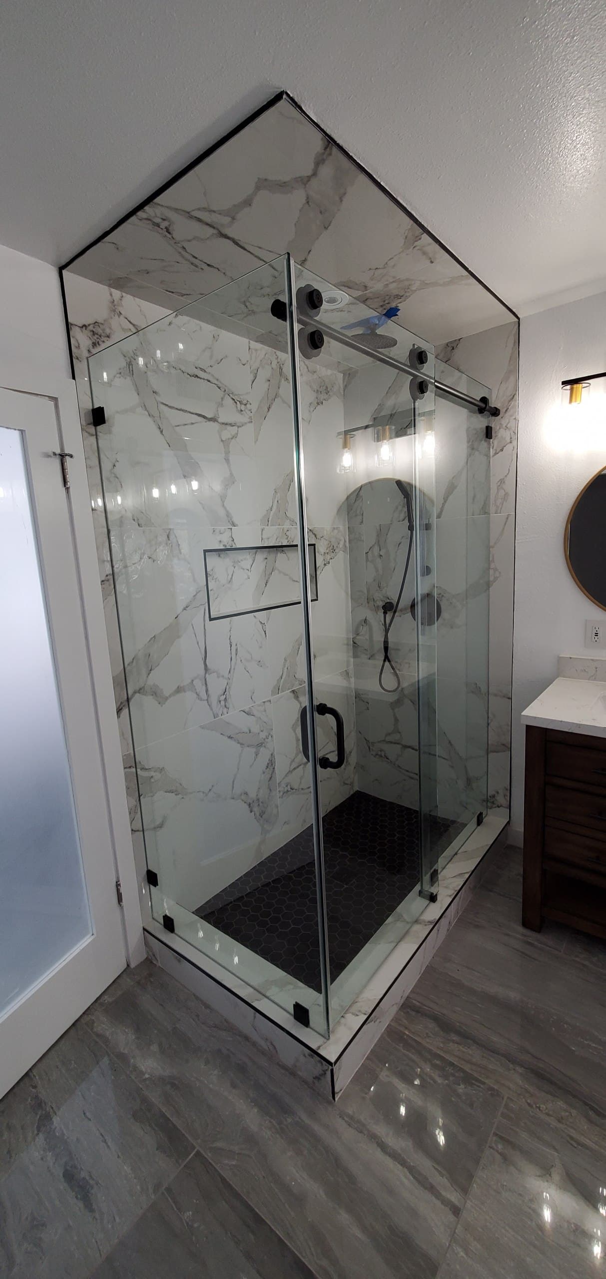 Frameless sliding shower enclosure with black hardware on Calacatta marble tile