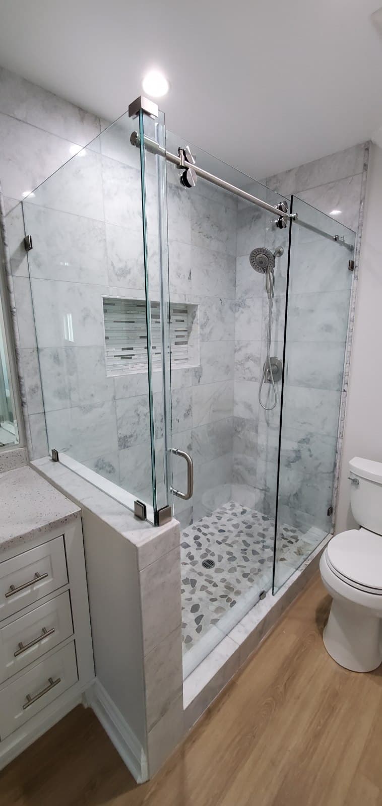 Brushed nickel sliding shower enclosure on Carrara marble with a pebble floor