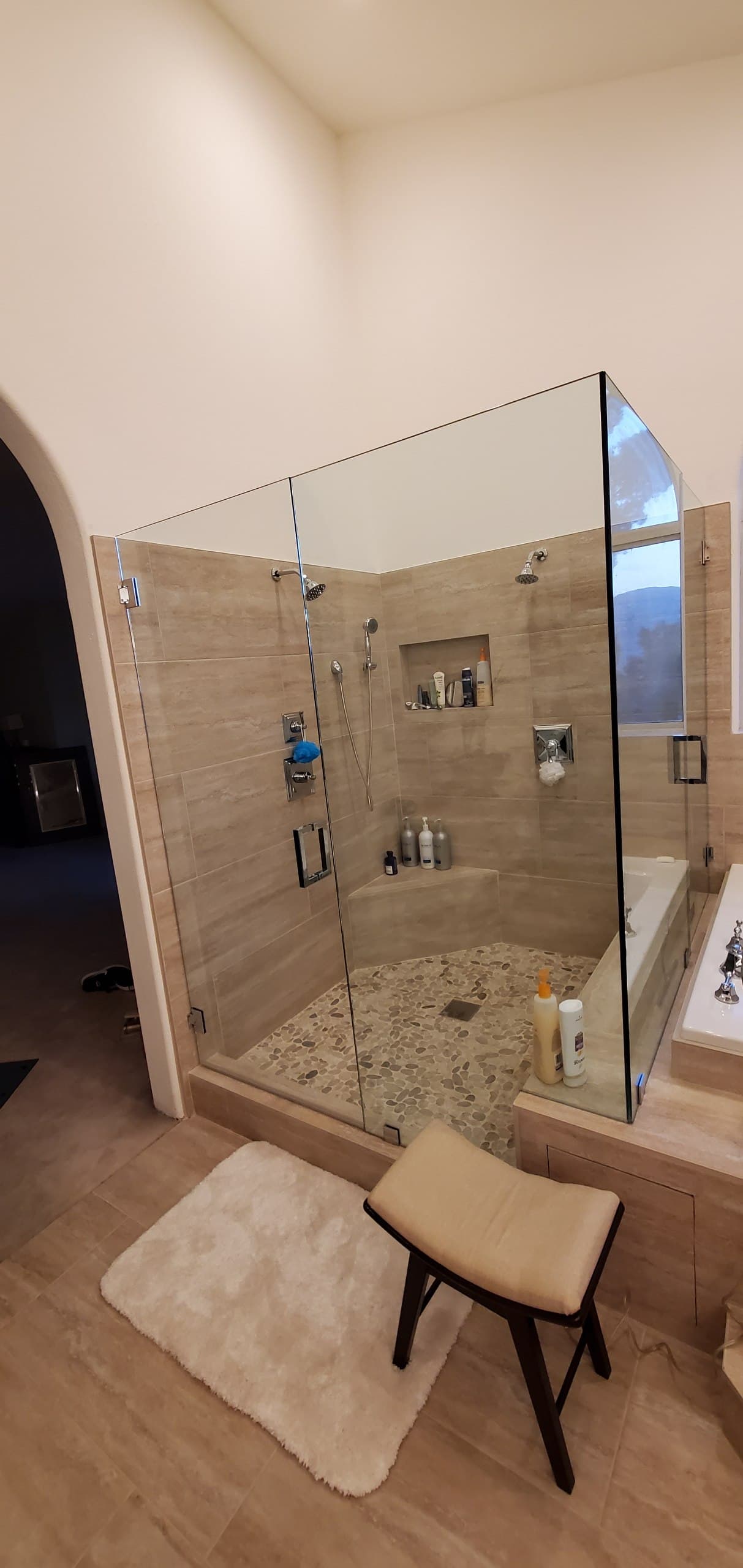 Frameless corner shower enclosure in travertine tile with a pebble floor and chrome hardware