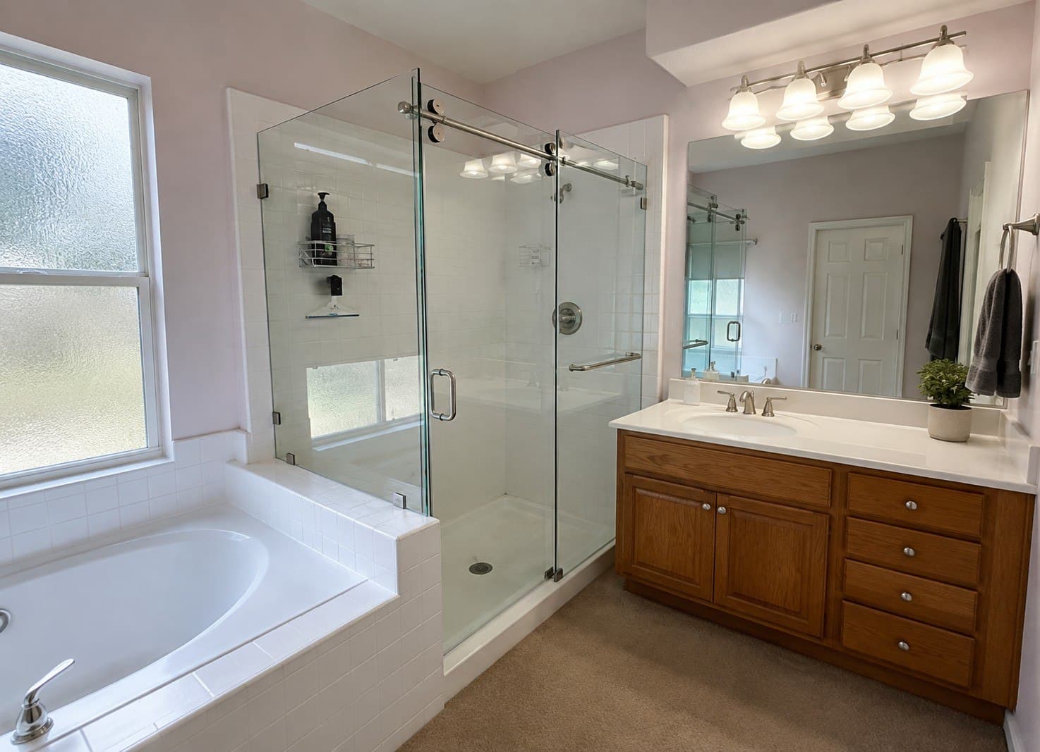 Sliding frameless glass shower enclosure on polished chrome barn-door hardware, over white tile beside a soaking tub